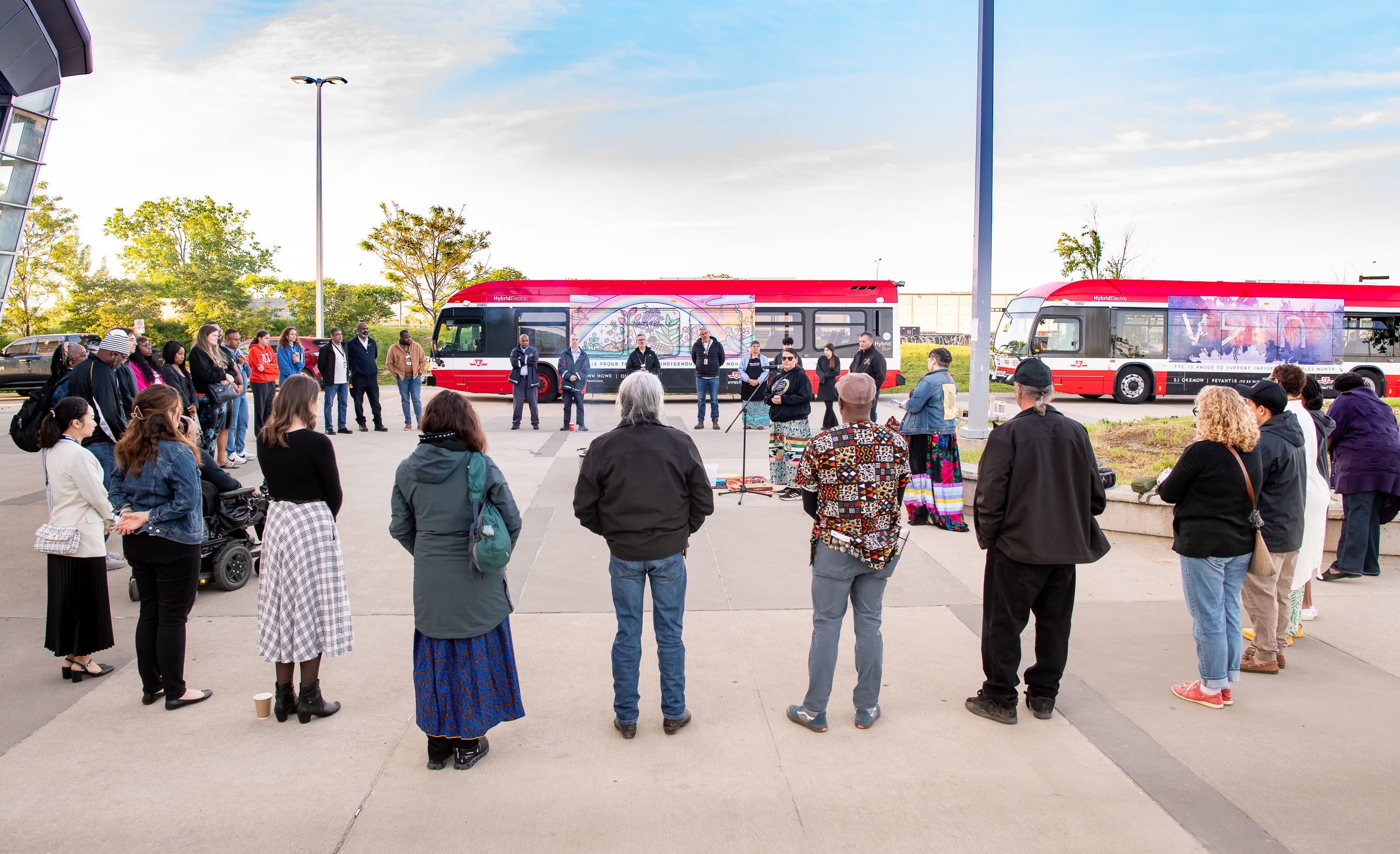 TTC employees and community members standing in a circle during a Sunrise Ceremony led by Indigenous Elders and Traditional Knowledge keepers. Special wrapped buses appear in the background.