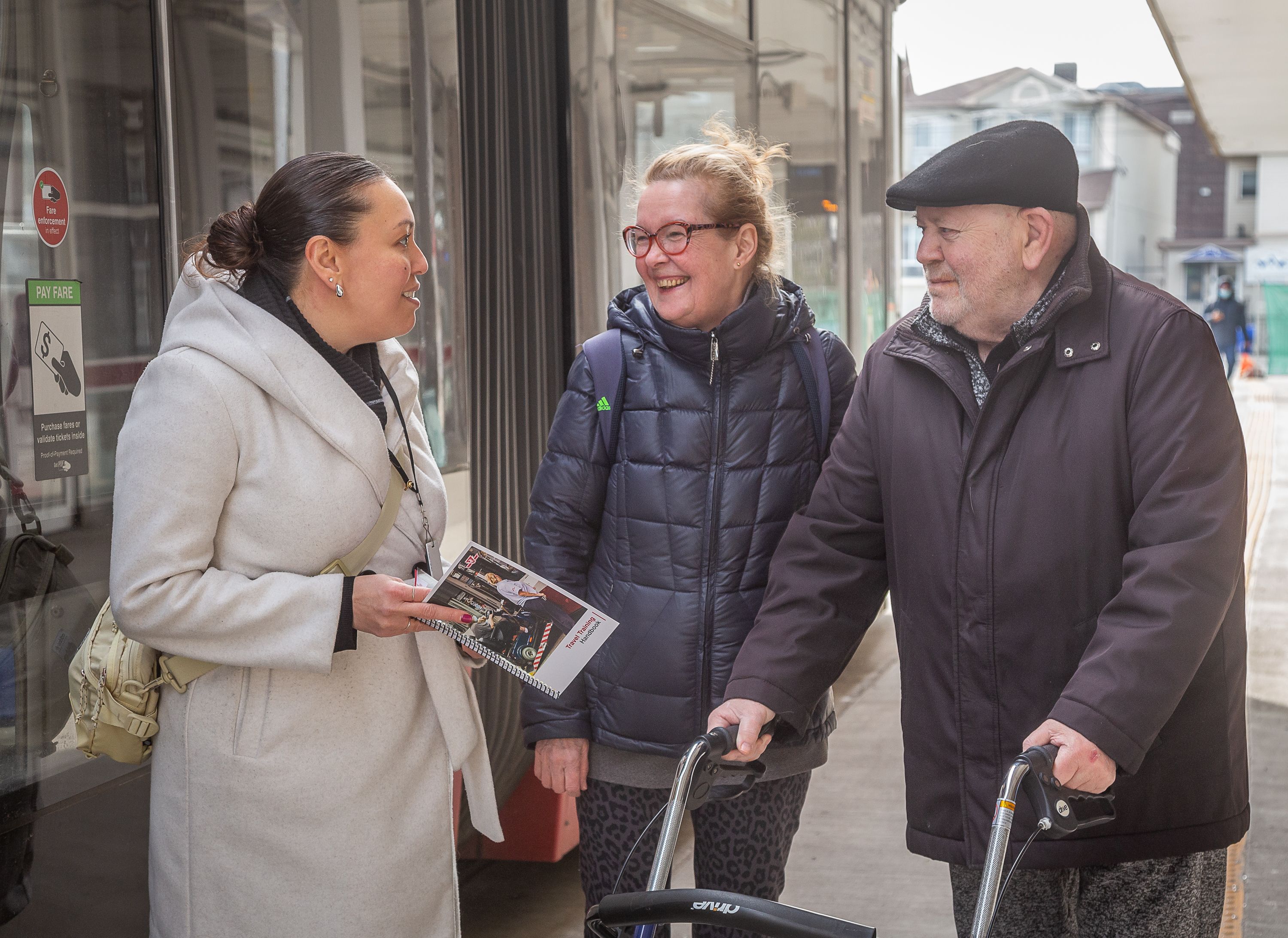 A TTC Travel Trainer is speaking to two Wheel-Trans customers at a streetcar stop during a Travel Training session.