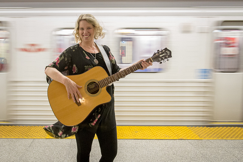 Kim Cole holding guitar on subway platform