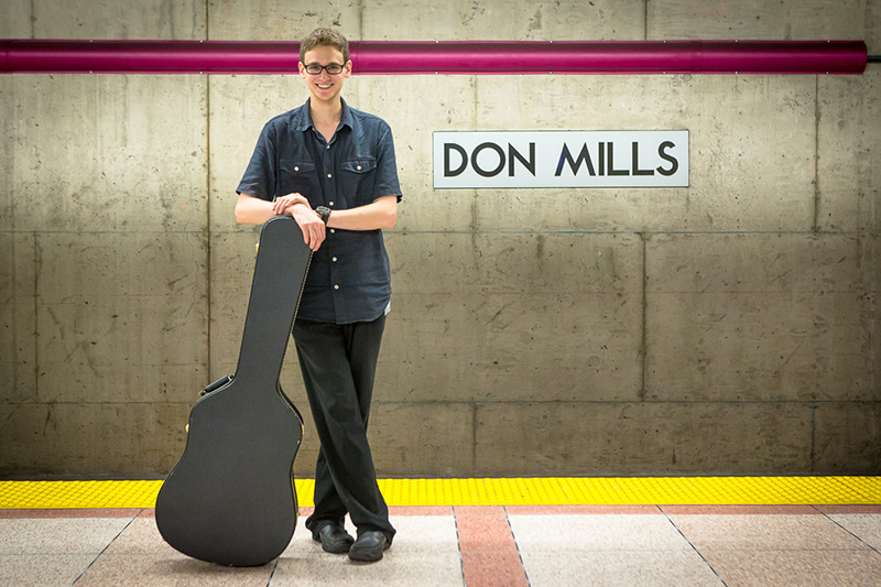 Jason Lane stands with his instrumnt on a subway platform.
