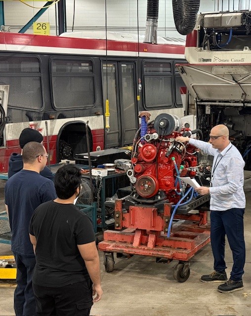 A group of TTC employees surrounding a bus engine.