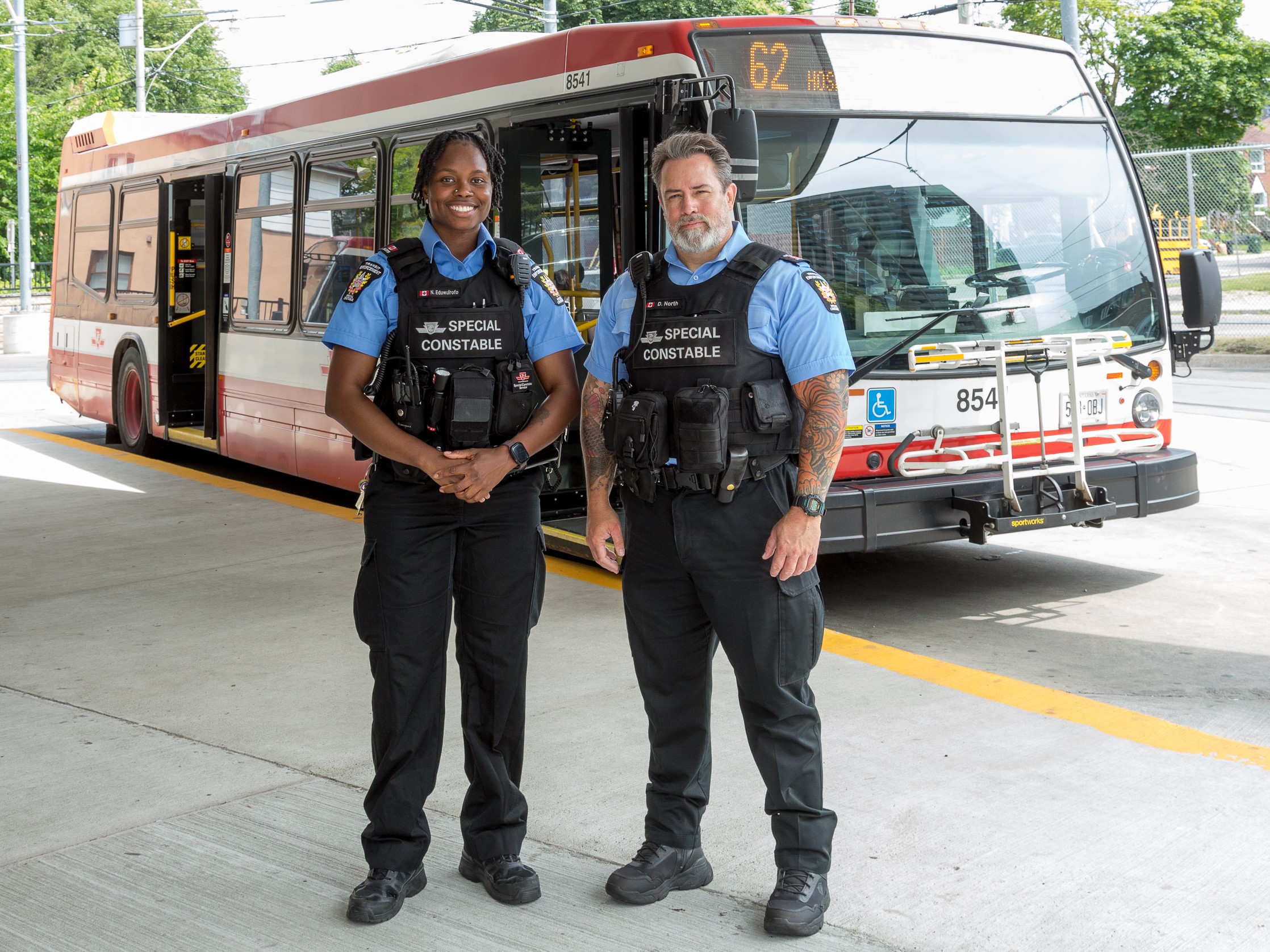 Two TTC Special Constables standing and smiling in front of a TTC bus.