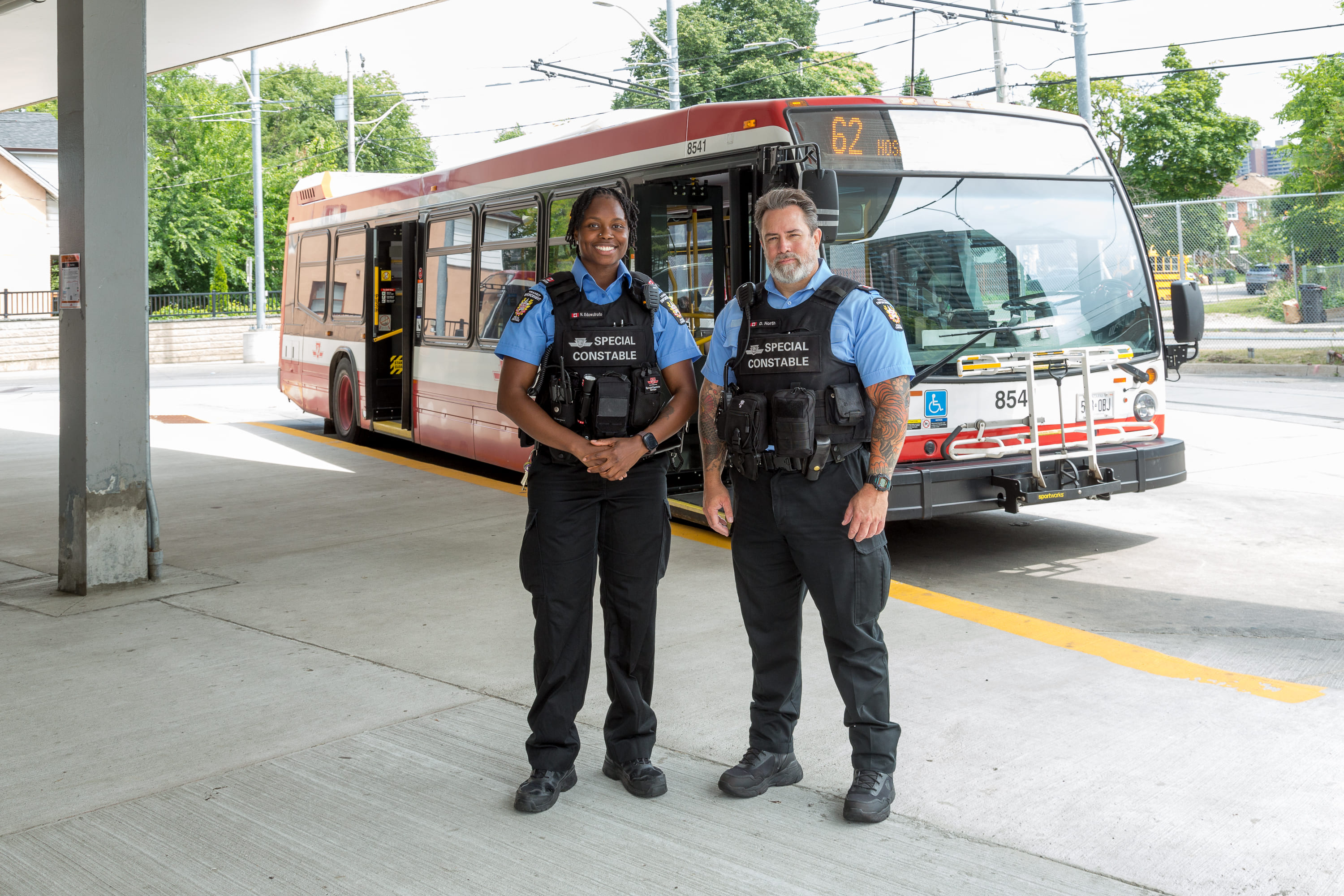 Two TTC Special Constables standing and smiling in front of a TTC bus.