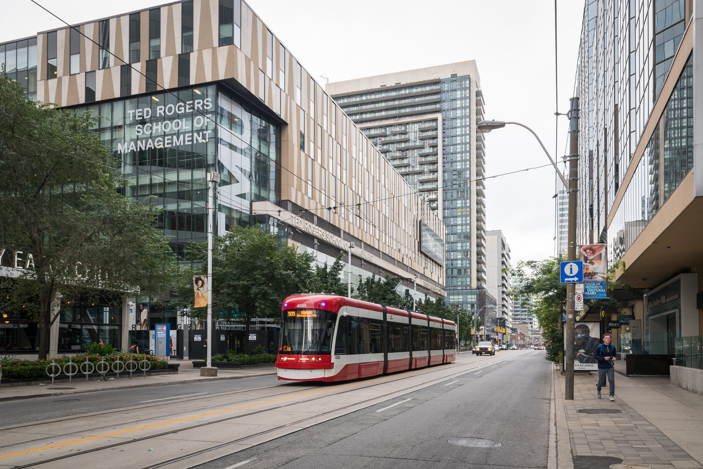 A red and white TTC streetcar passing by the Ted Rogers School of Management building.