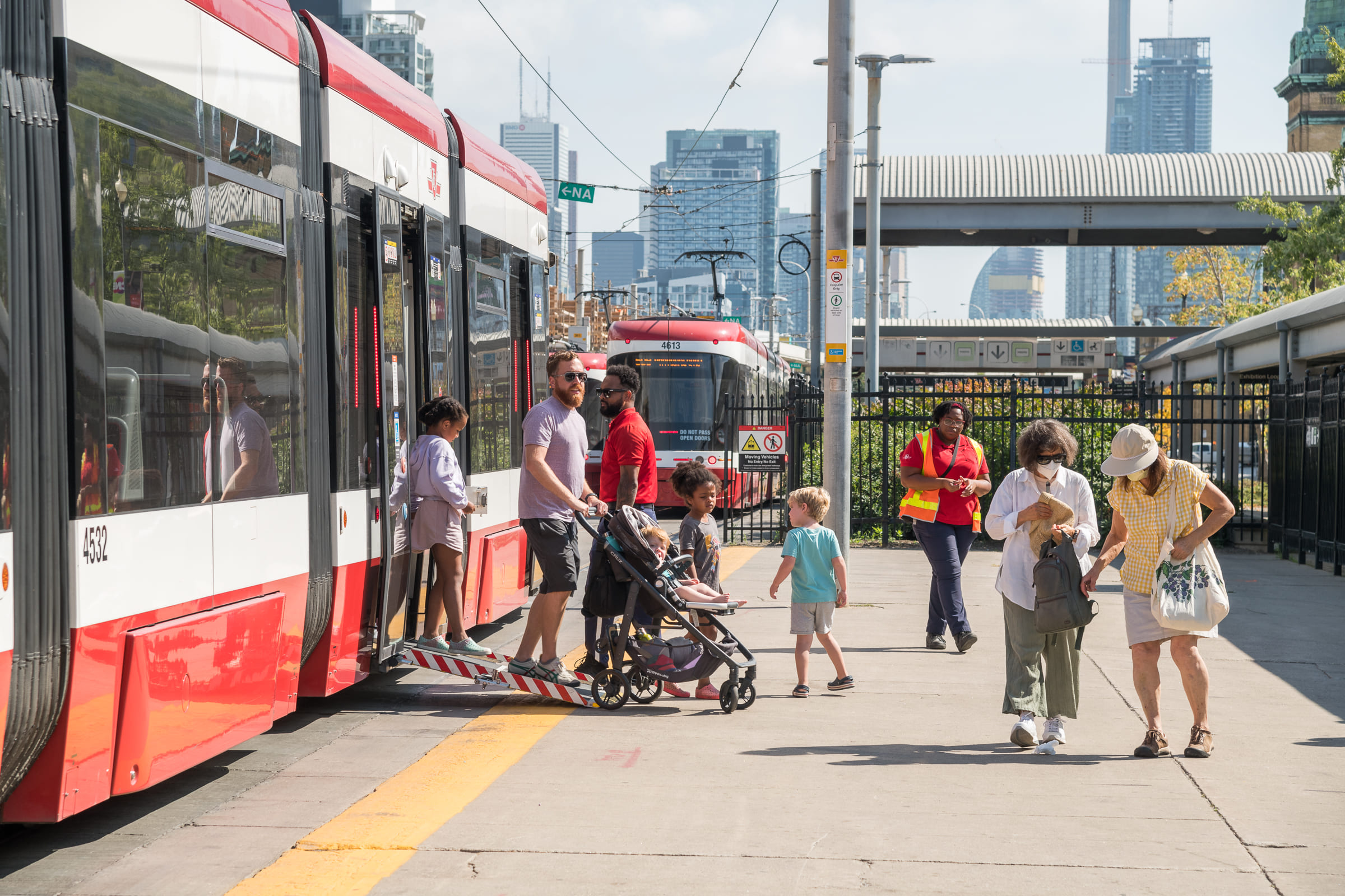 People getting off a red and white TTC streetcar with buildings visible in the background.