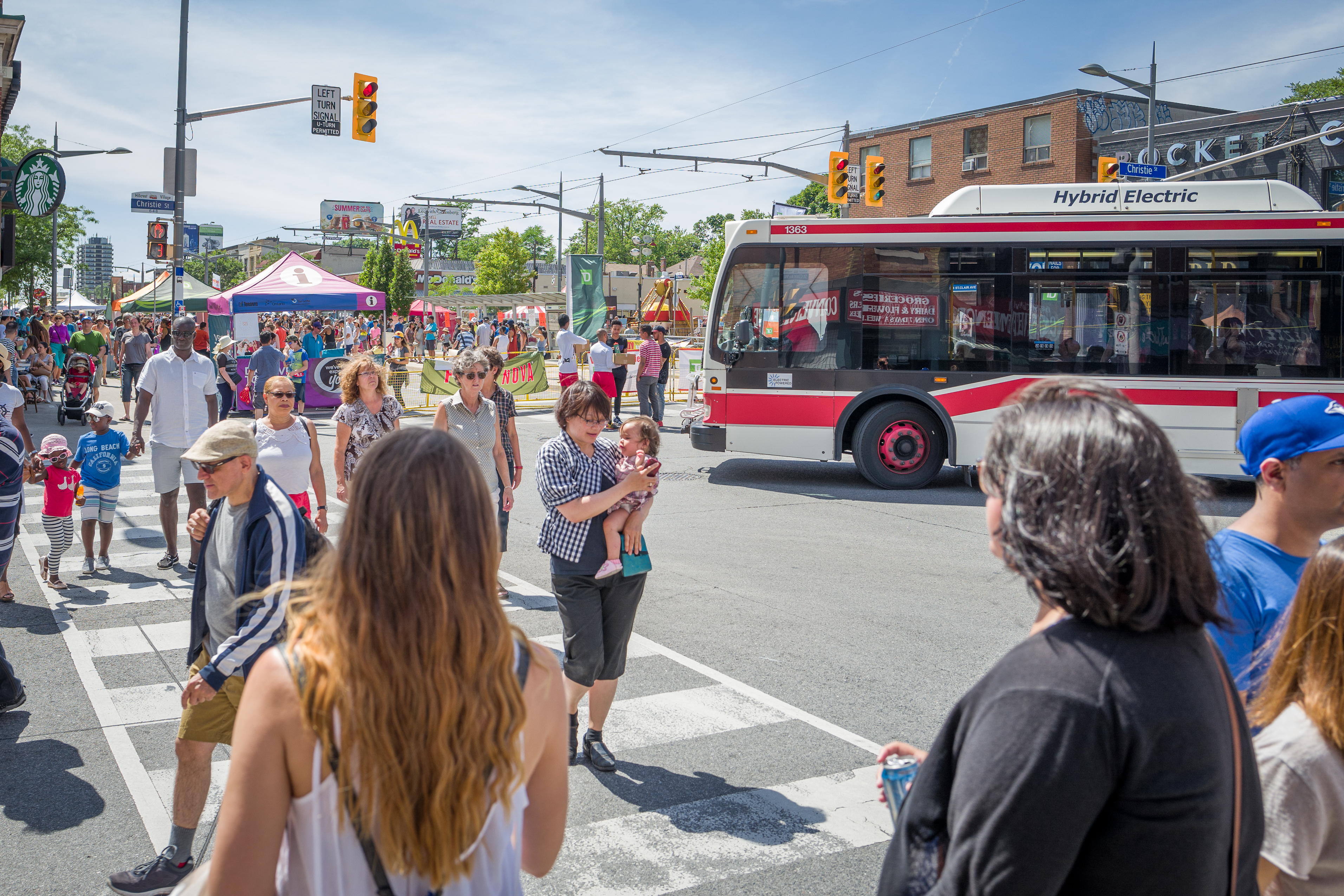 Large crowd of people at a street festival with a TTC bus in the background.