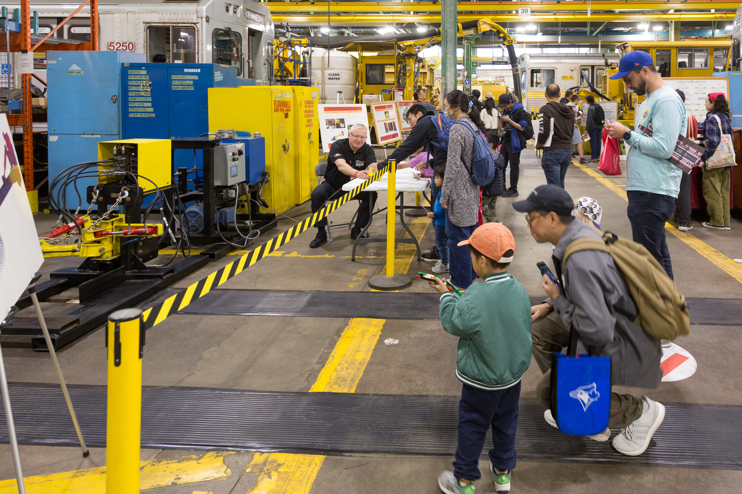 Families exploring the TTC Open House at Greenwood Yard, with visitors gathered near a display table and maintenance equipment.