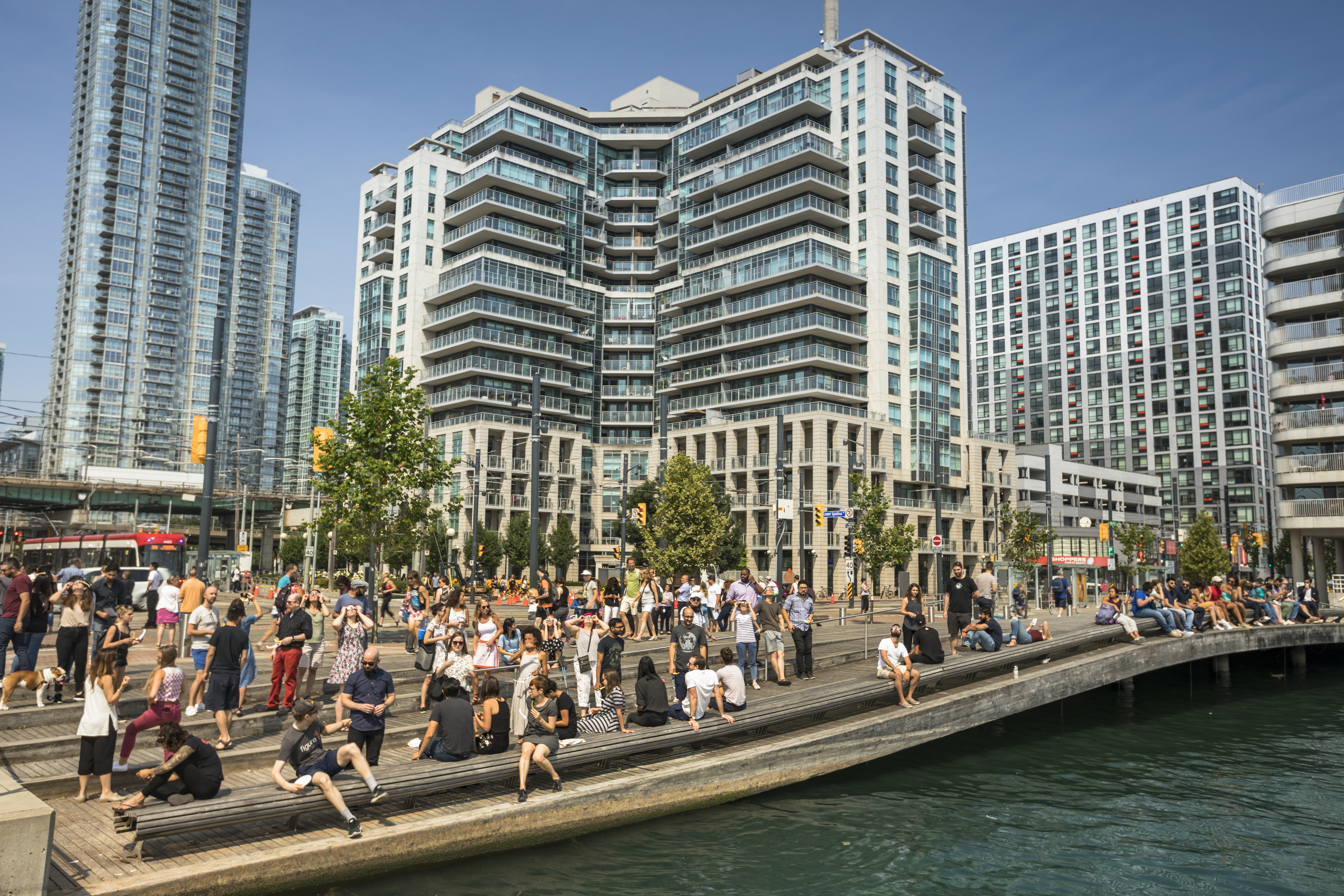 A large group of people relaxing at the Harbourfront with tall buildings and a red and white TTC streetcar in the background.