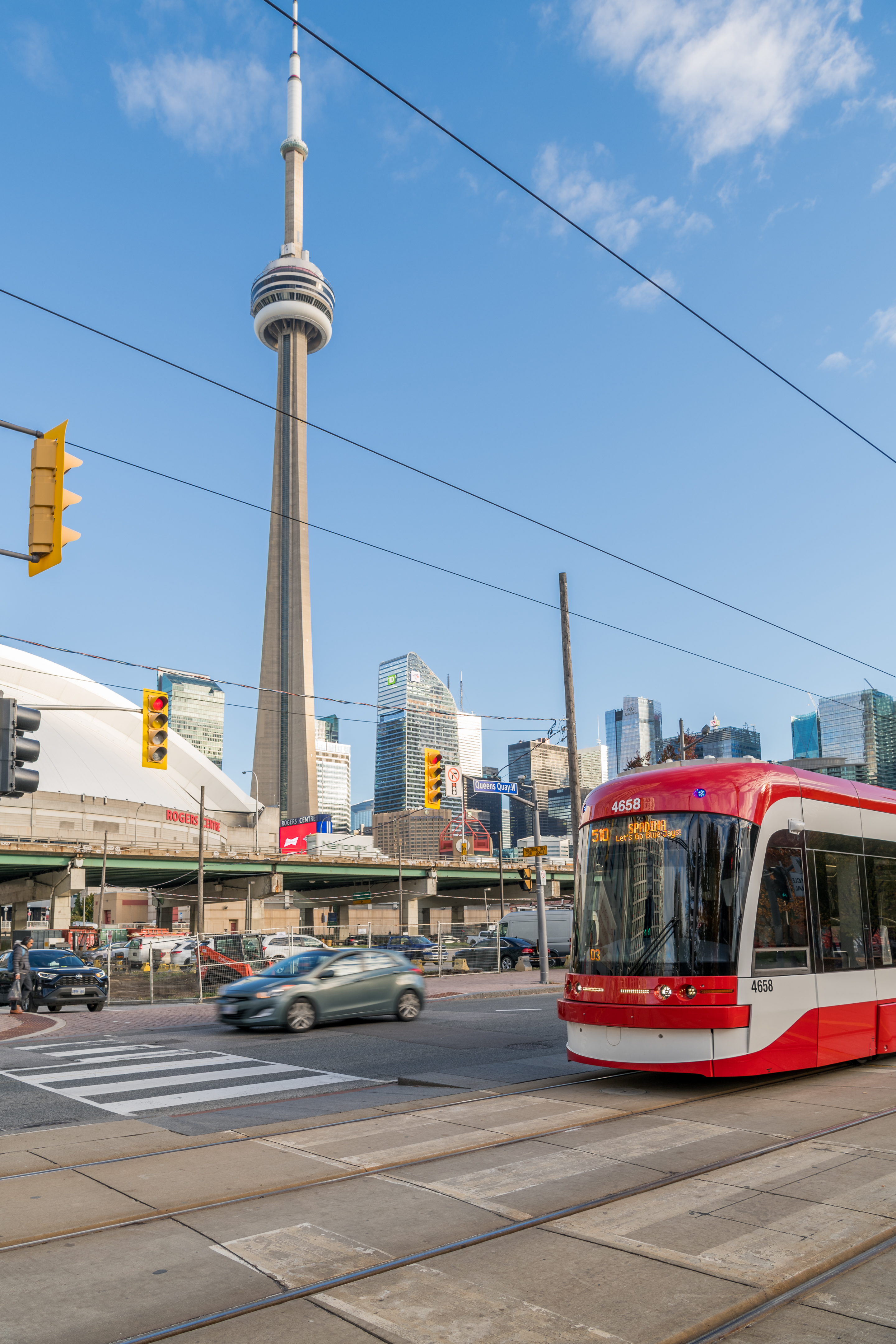 A red and white TTC streetcar on Queens Quay West with the CN Tower and Rogers Centre in the background.