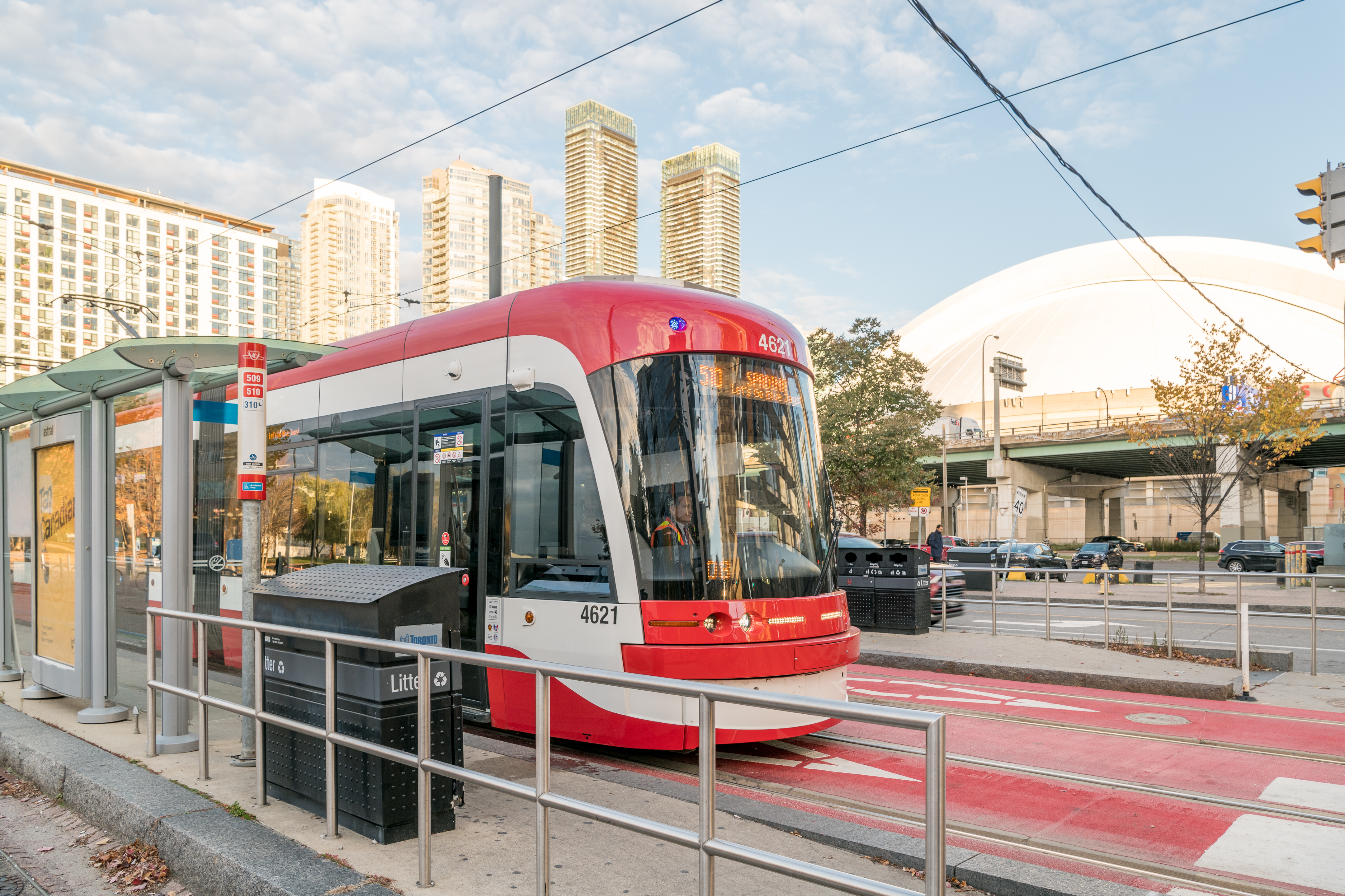 A red and white TTC streetcar at an outdoor stop in front of the Rogers Centre and tall buildings.