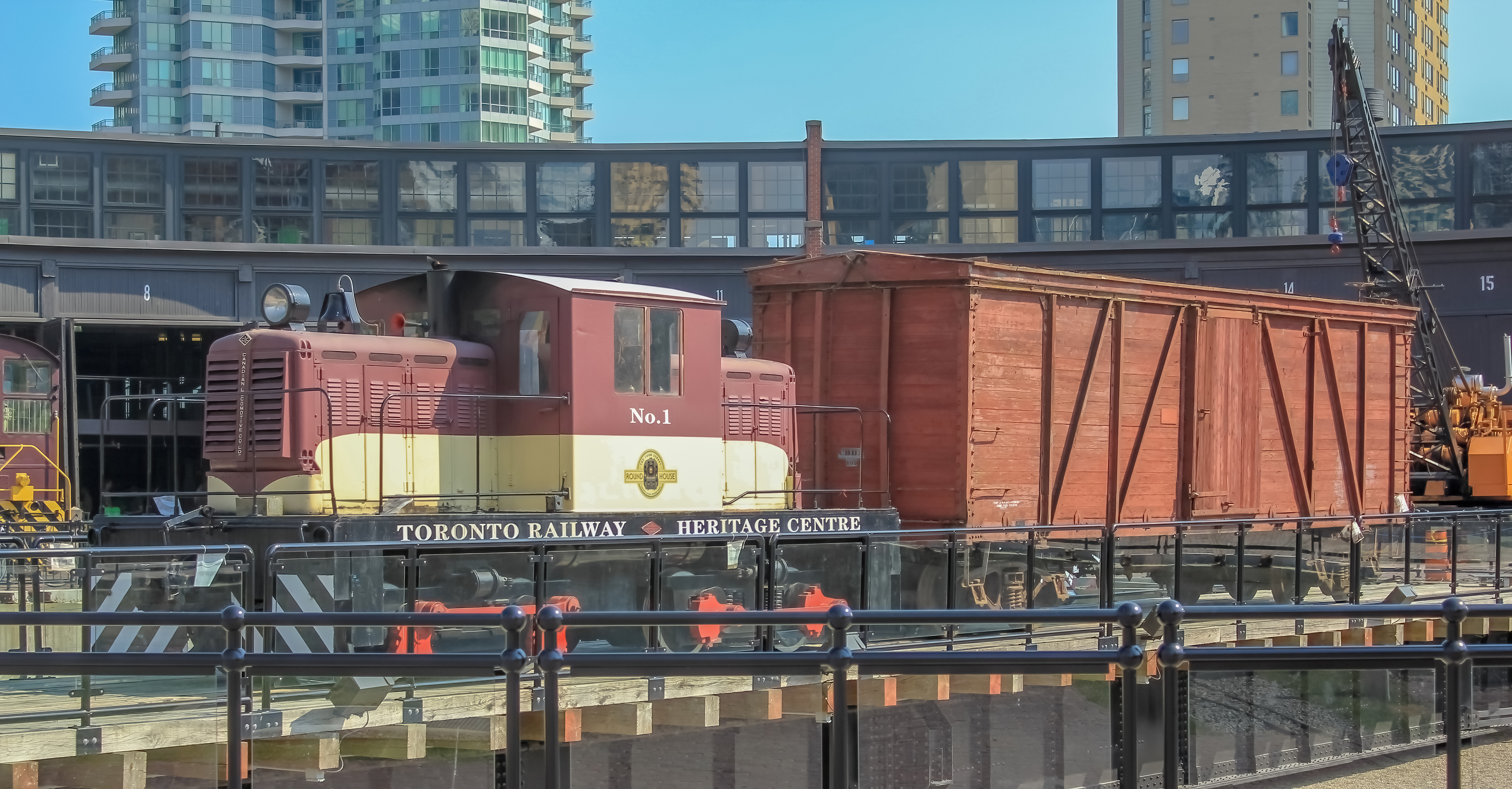 A vintage brown and yellow train in front of a black curved building at the Toronto Railway Heritage Centre.