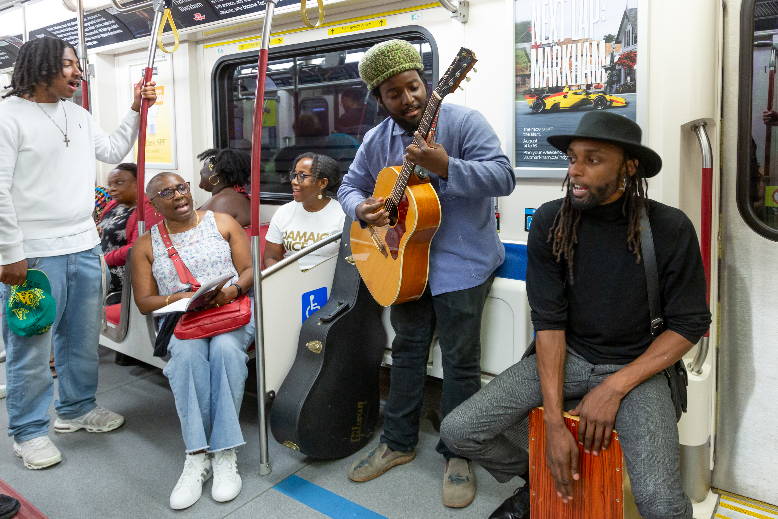 People on a TTC subway train sit and stand next to a person playing a guitar and a person drumming.