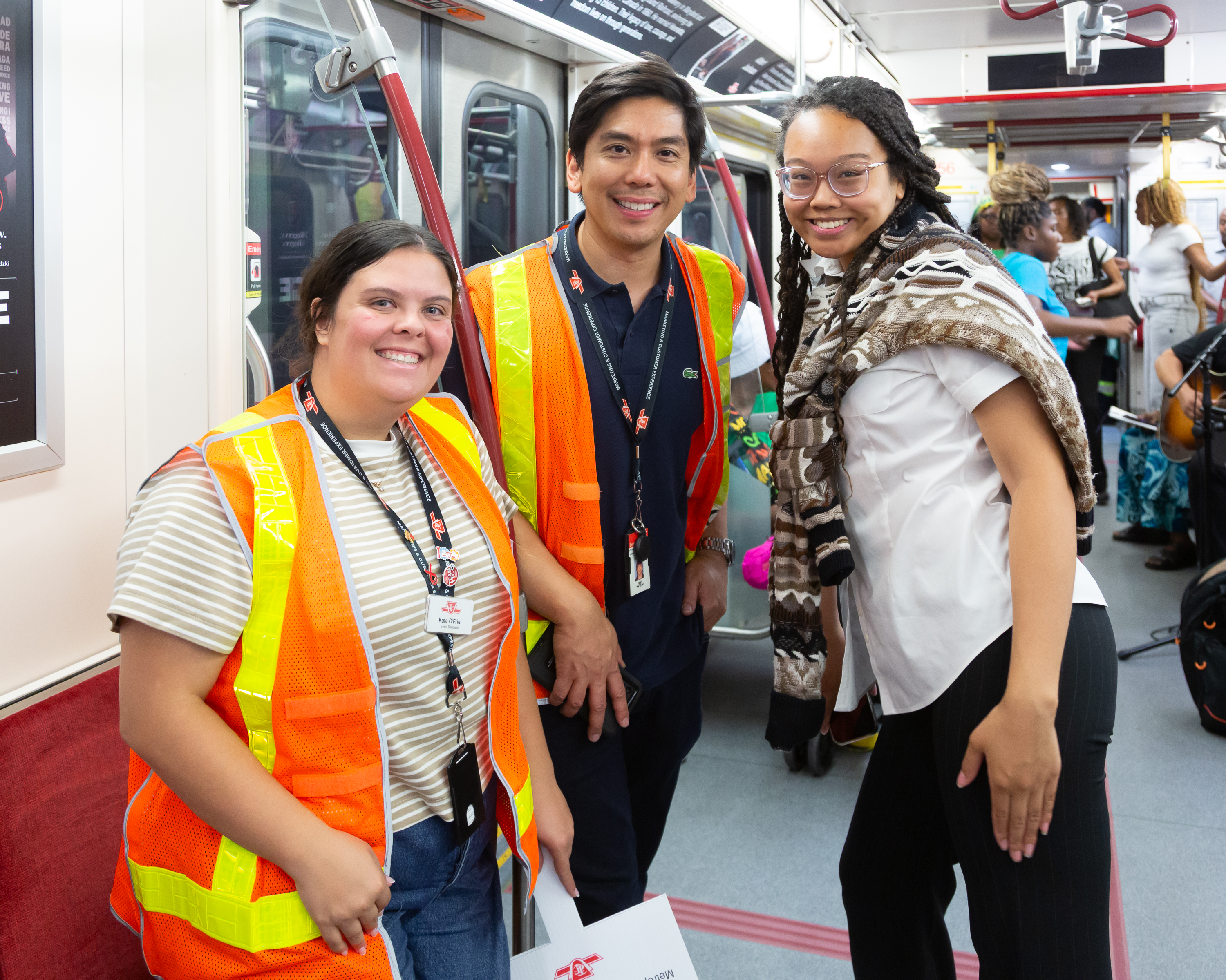 Three TTC employees standing and smiling. Two are wearing bright orange and yellow vests.
