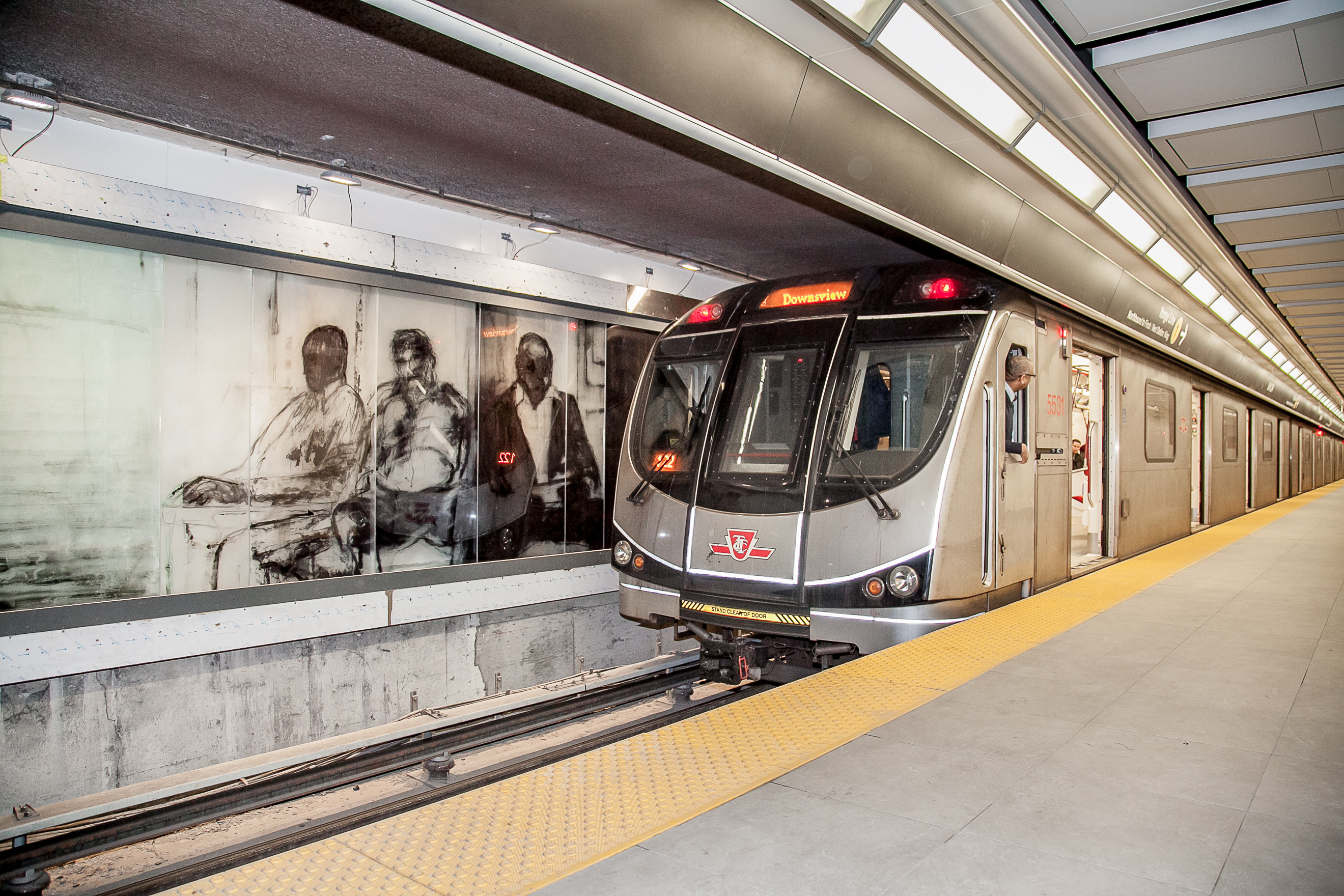 A stopped TTC subway train at the Union Station platform next to the translucent glass commuter artwork wall.