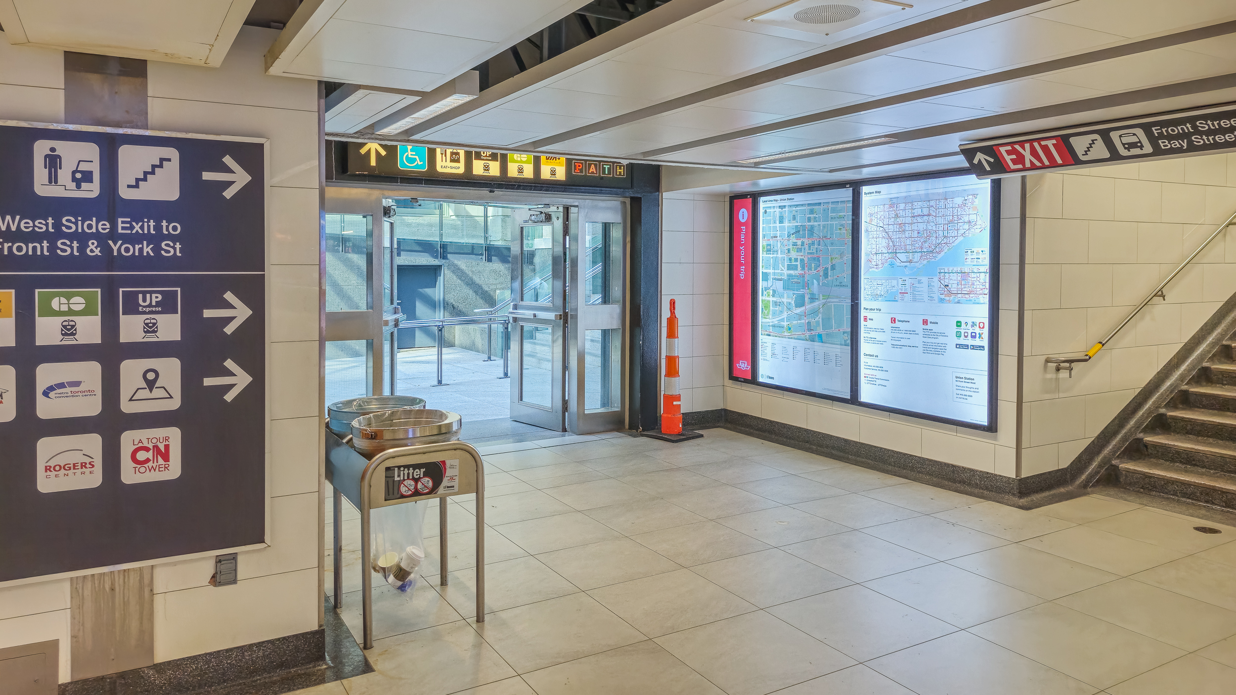 Current day TTC Union Station concourse with signage, exit doors, transit map, and a staircase with a rail.