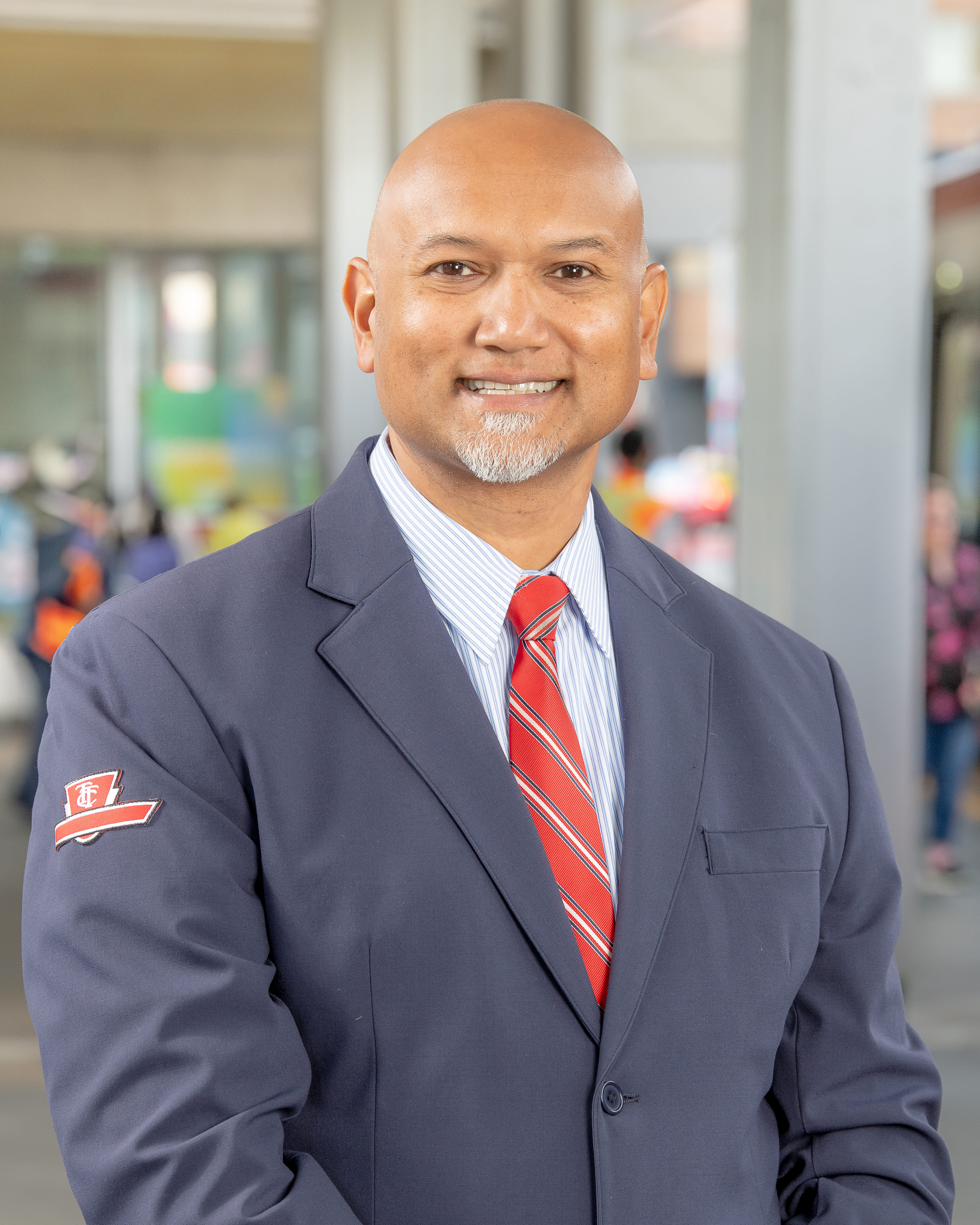A TTC subway operator smiling in a blue blazer with a TTC logo on the arm and red tie.