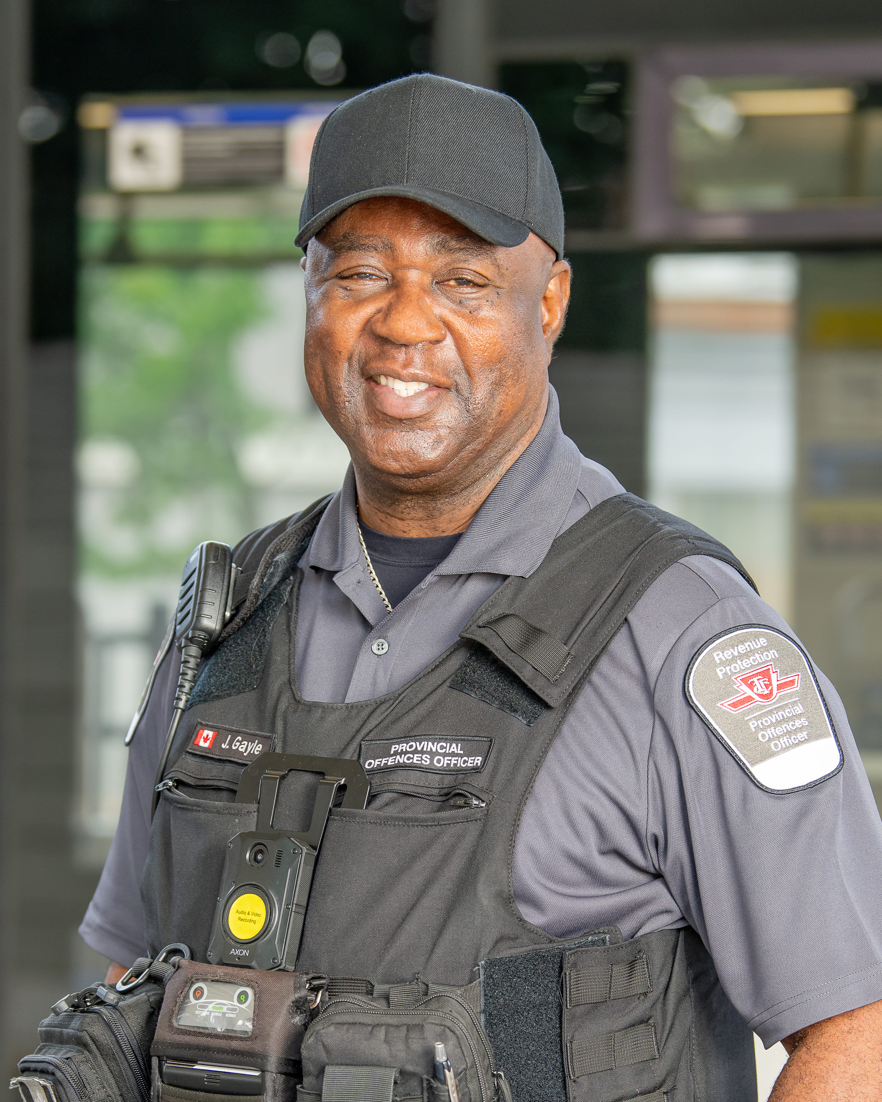 A Provincial Offences Officer smiling in a black vest, grey shirt and black hat.