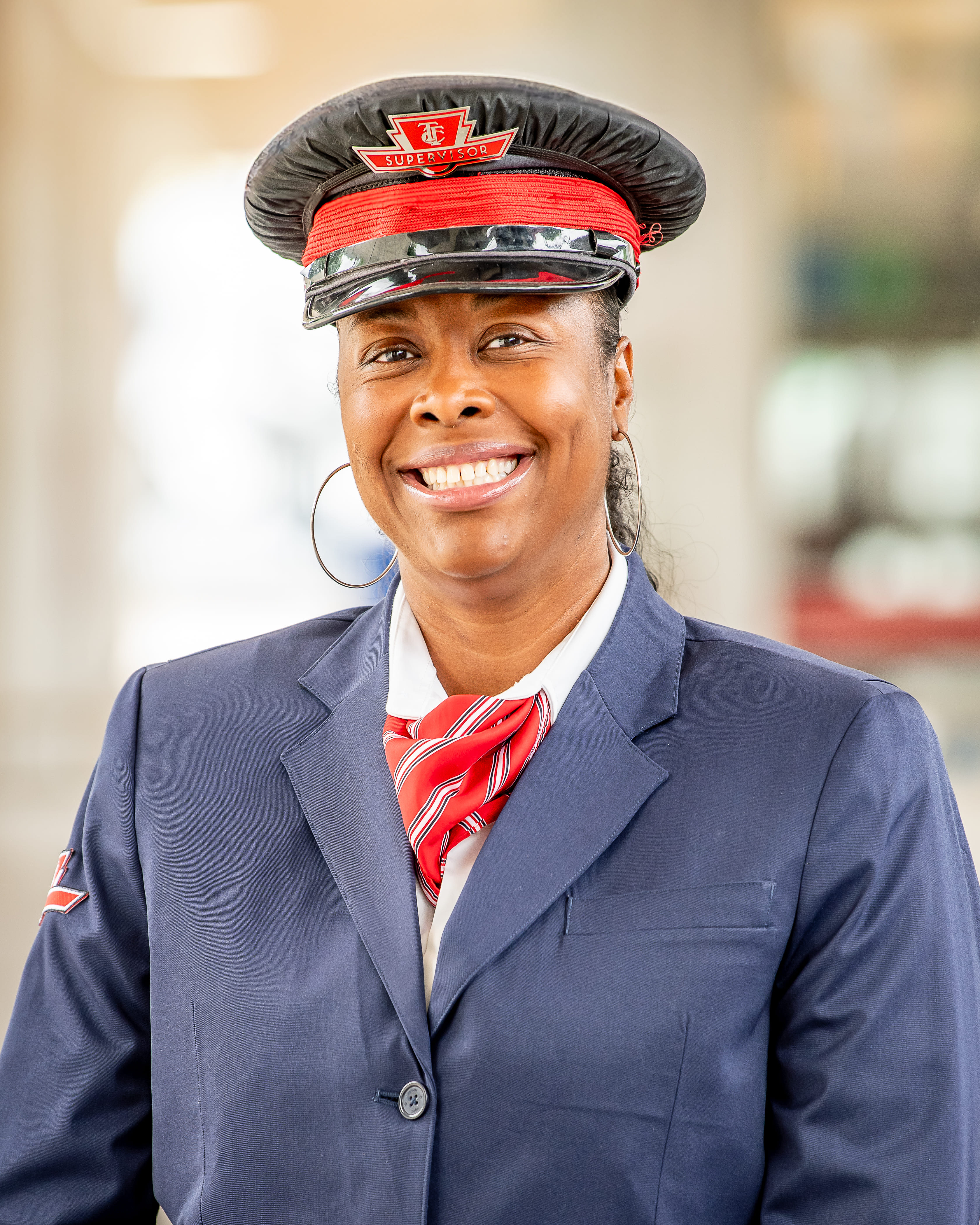 A TTC operations supervisor smiling in a blue blazer with a TTC logo on the arm, a red tie and a red and black hat with the TTC logo.