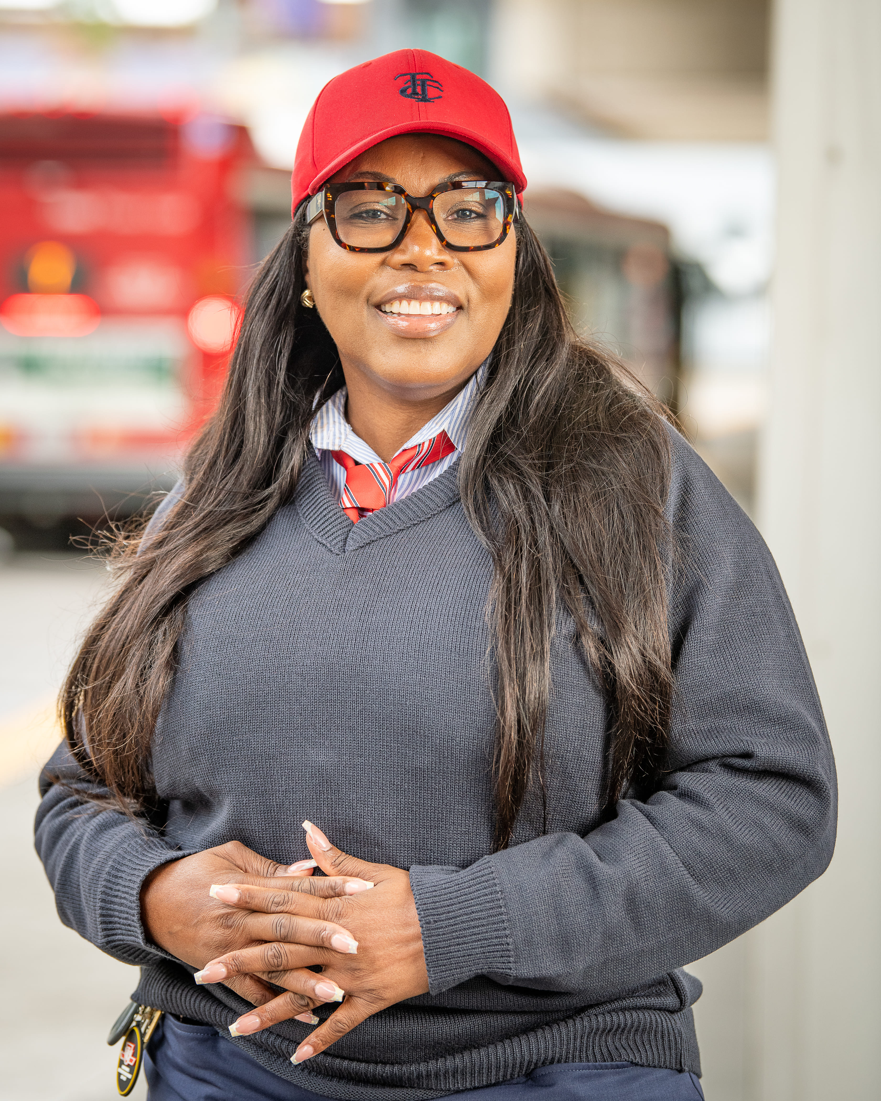 A TTC bus operator smiling in a blue v-neck sweater, red tie and red hat with a black TTC logo.