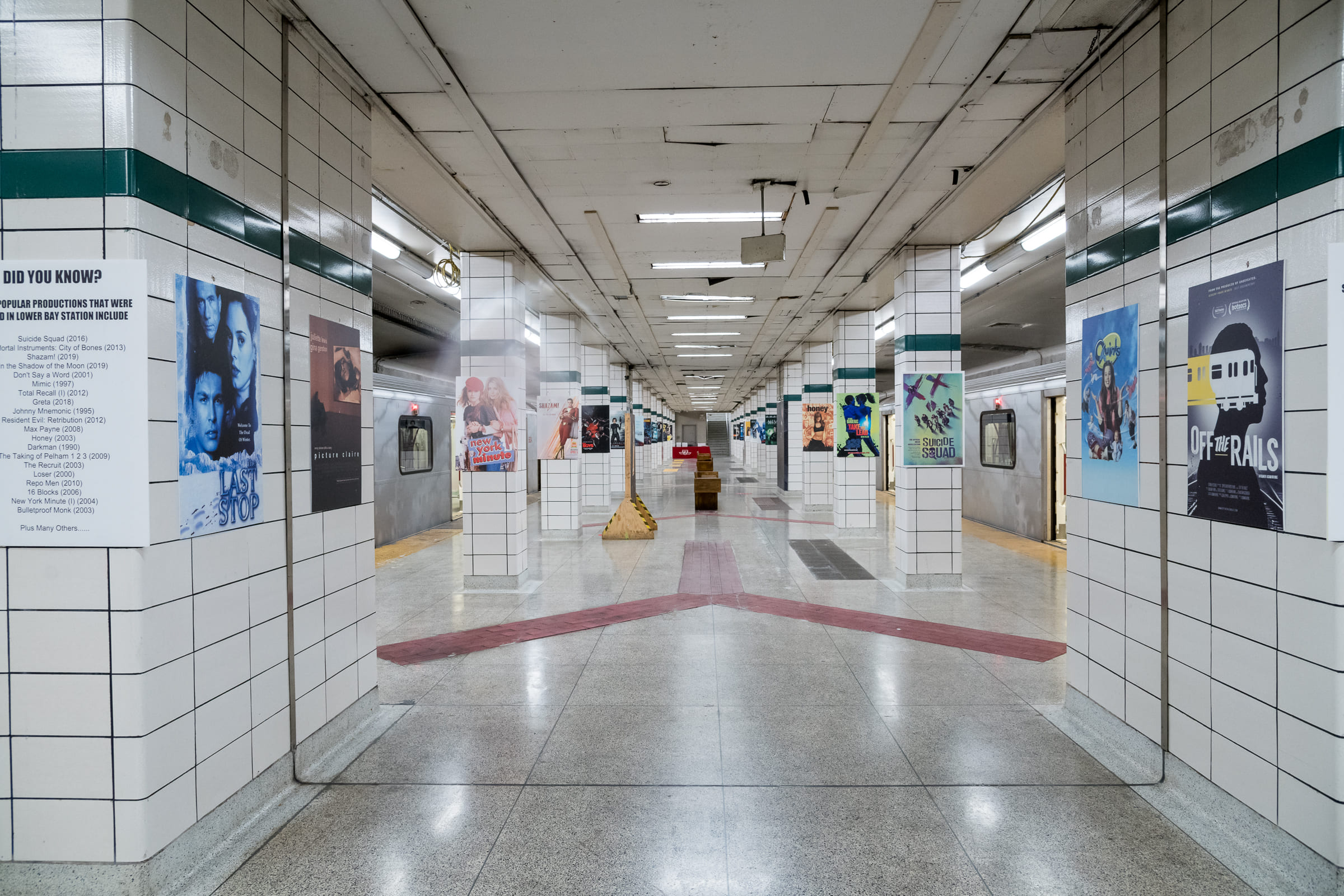 An empty subway station with trains on both platforms and posters on the interior columns.