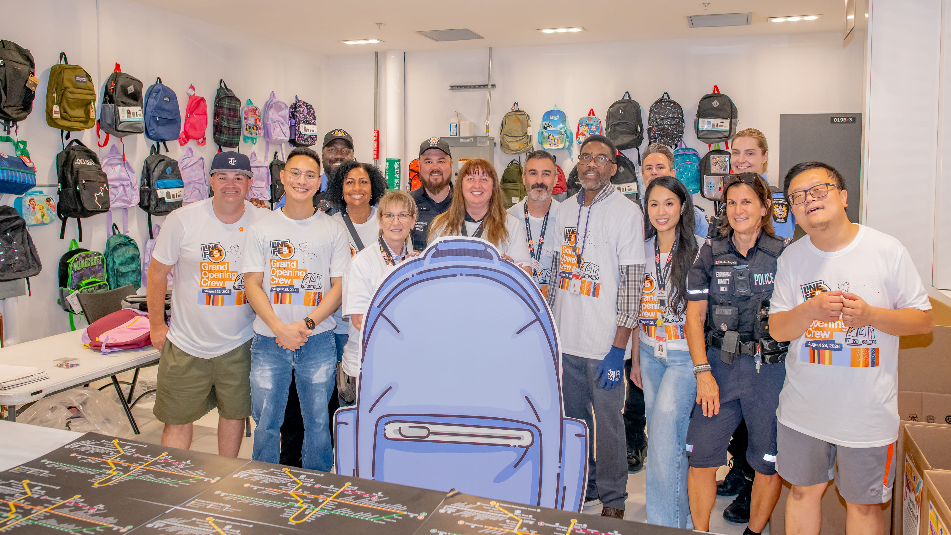 TTC staff pose for a photo around a backpack cutout with donated backpacks hanging in the background, to celebrate the final day of the TTC Backpack Drive