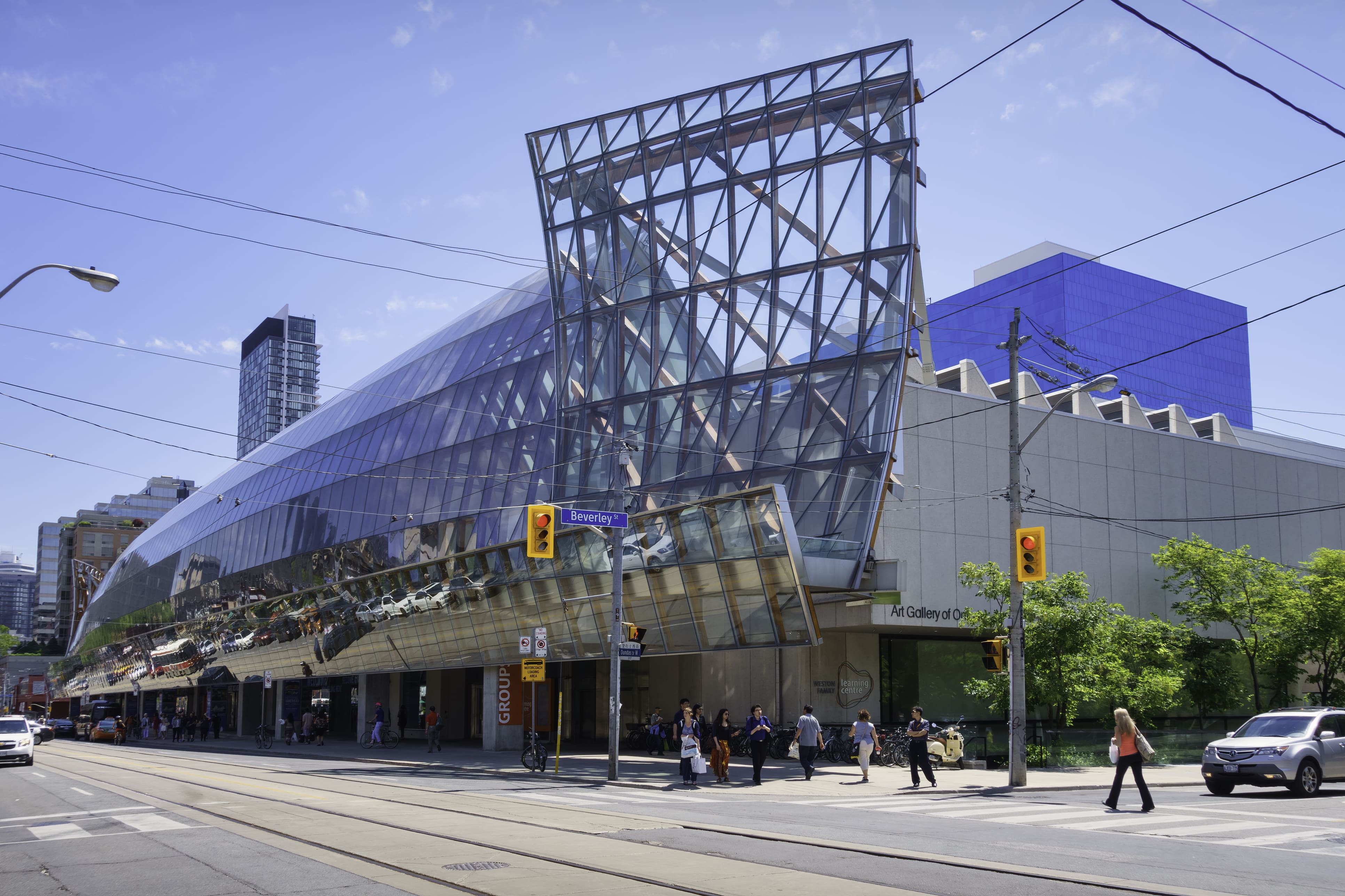 An exterior shot of the Art Gallery of Ontario, a large, angular glass building. People are walking in front.