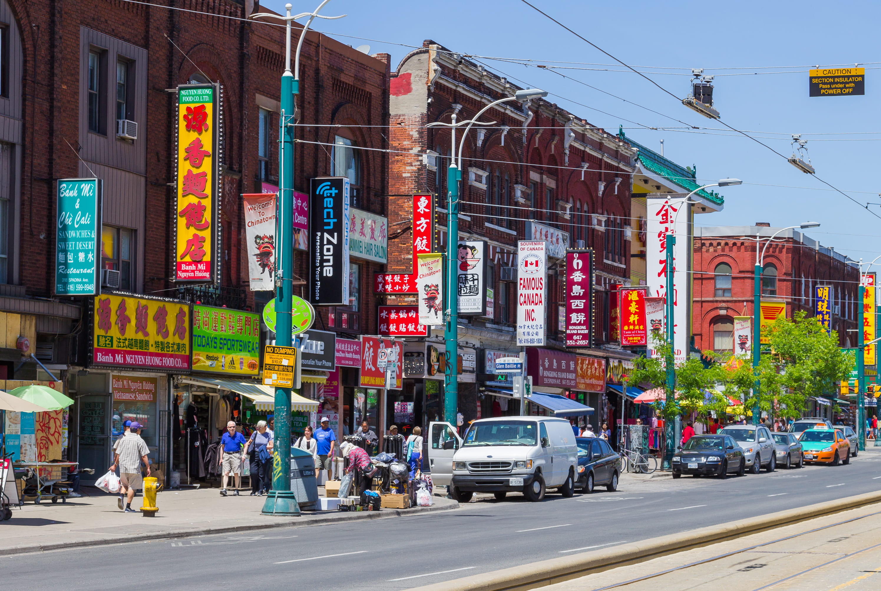 Spadina Avenue in Toronto during the day with people, cars and colourful storefronts.