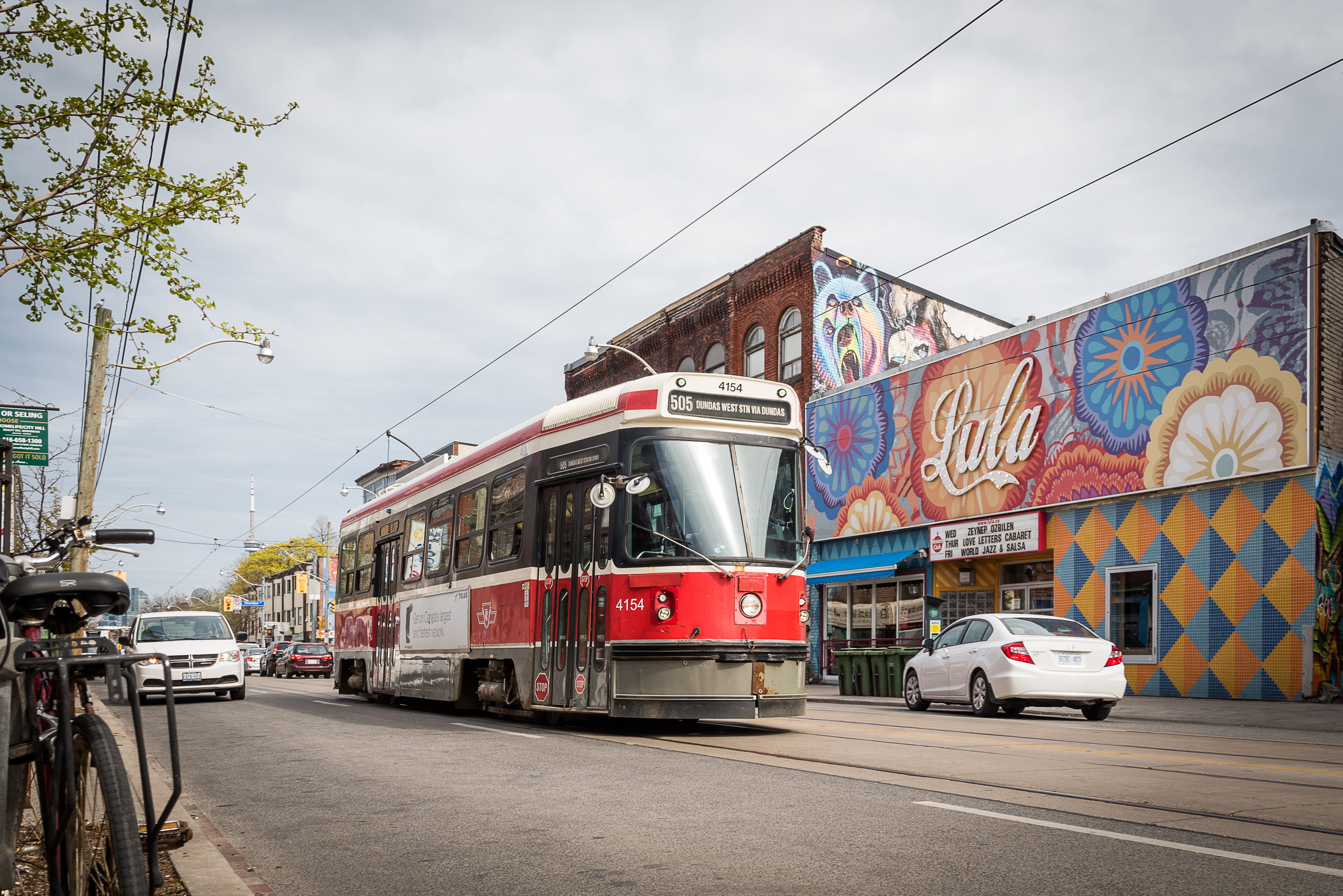 A red and white TTC streetcar on the street with cars passing on both sides.