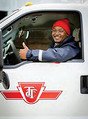 A worker smiles and motions a thumbs up, while sitting inside of a TTC vehicle.
