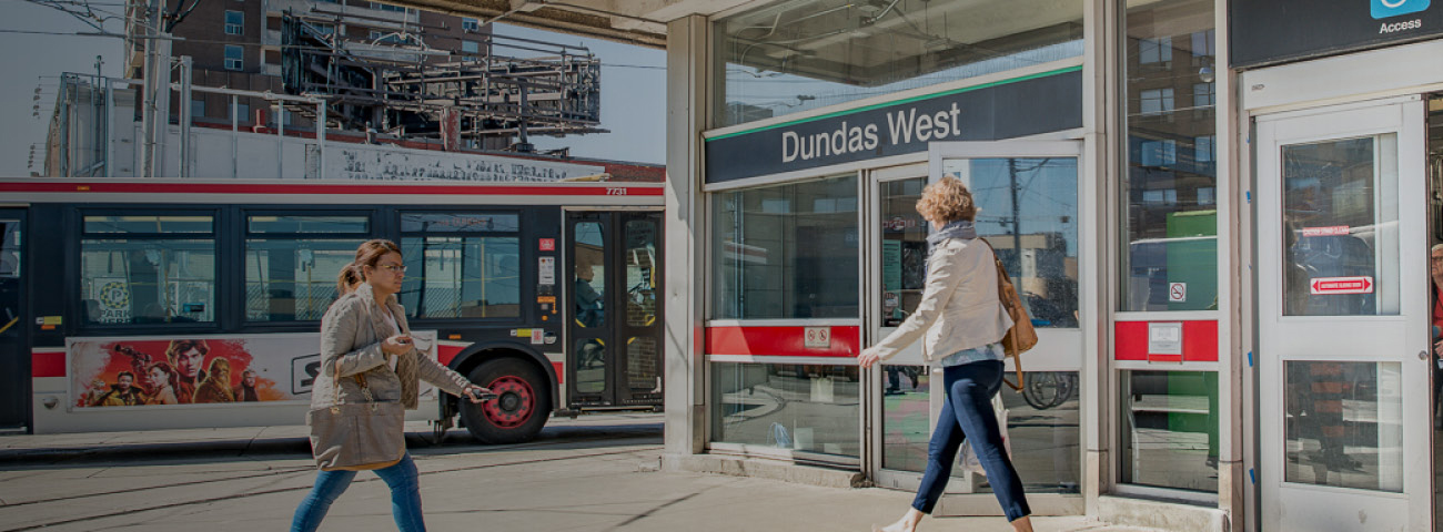 people exiting and entering Dundas West Station, also nearby a bus is waiting for passengers.
